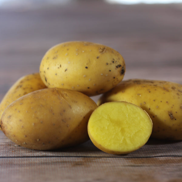 Three yellow potatoes with one cut in half on a wooden surface