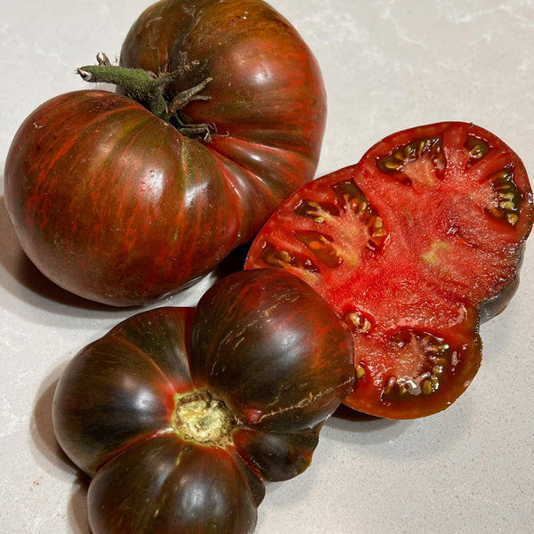 Three dark red tomatoes on a light gray surface, with one sliced open to show interior.