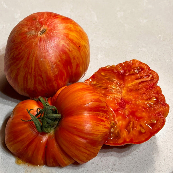 Two whole tomatoes and one cut in half on a white surface