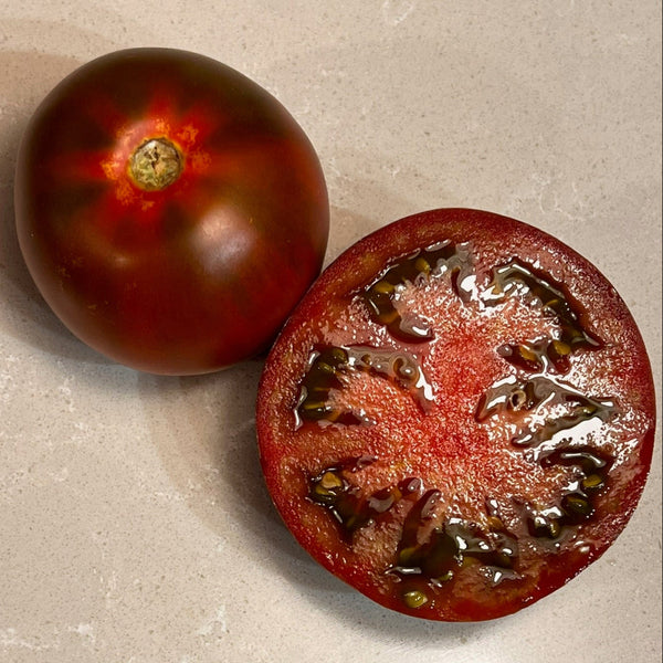 Whole and halved dark chocolate tomato on a textured surface with a label reading 'Dark Chocolate'.